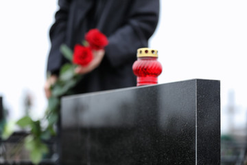 Woman with red roses outdoors, focus on candle. Funeral ceremony