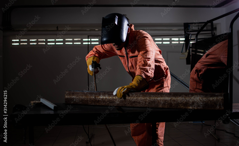 Wall mural a man wearing safety mask and suit is welding metal