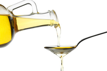Pouring cooking oil from jug into spoon on white background