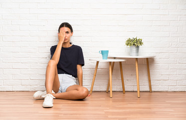 Young woman sitting on the floor covering a eye by hand