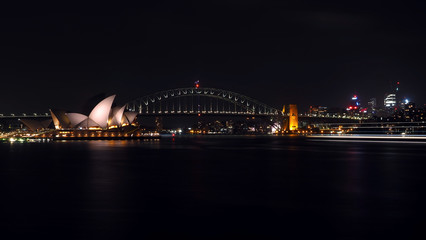 Fototapeta na wymiar Beautiful long exposure shot of Sydney Opera House and Sydney Harbour Bridge at night with a light trail of passing ferry.