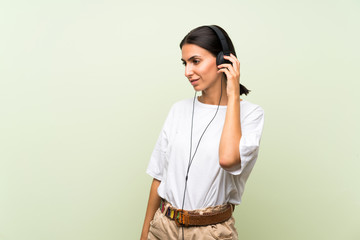 Young woman over isolated green background listening to music with headphones