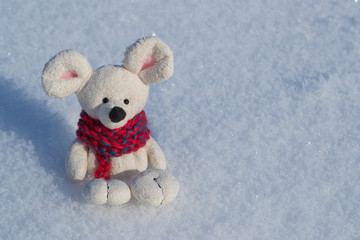 Christmas toy mouse, a symbol of the Chinese New Year. In a red knitted scarf. Against the background of white snow. Space for text.