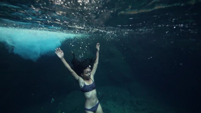 A young skinny woman in bikini floating underwater and holding her breath.