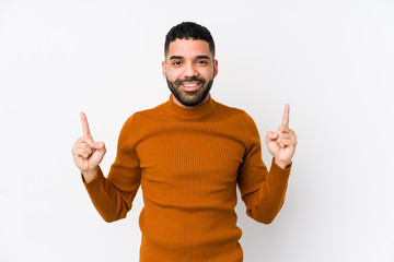 Young latin man against a white background isolated indicates with both fore fingers up showing a blank space.