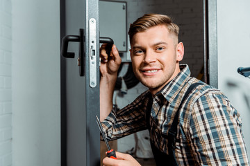 cheerful installer holding screwdriver while touching door handle
