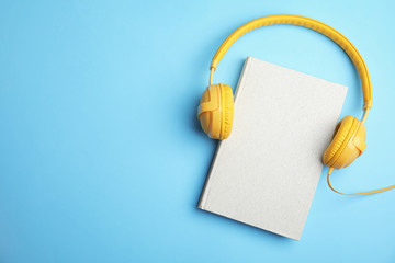 Book and modern headphones on light blue background, top view. Space for text