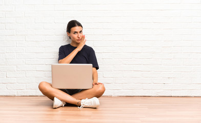 Young woman with a laptop sitting on the floor whispering something