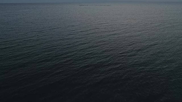 Aerial video of endless, blue, empty sea or ocean water surface at sunset. Pedestal shot, drone camera ascends slowly above water.