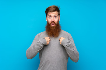 Redhead man with long beard over isolated blue background with surprise facial expression