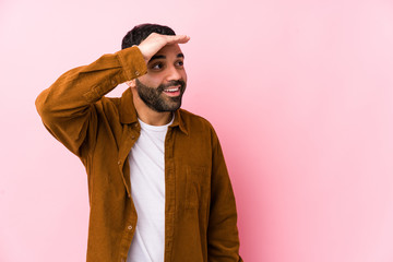 Young latin man against a pink background isolated looking far away keeping hand on forehead.