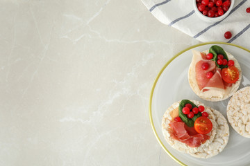 Puffed rice cakes with prosciutto, berries and basil on grey marble table, flat lay. Space for text