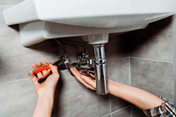 cropped view of installer holding pliers near pipe in bathroom