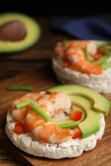 Puffed rice cakes with shrimps and avocado on wooden board, closeup