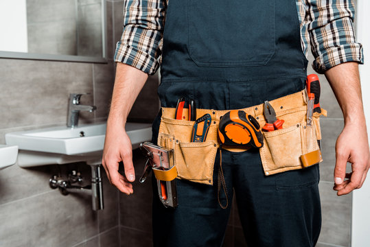 cropped view of installer with tool belt standing in bathroom