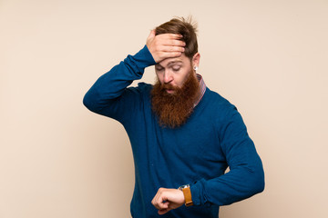 Redhead man with long beard over isolated background with wrist watch and surprised