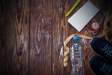 Healthy lifestyle and sports background. Sports shoes, Notepad and pen, stopwatch and water bottle on wooden background with copyspace, top view.