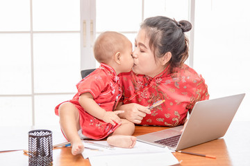 Young Asian working women sitting and kissing her baby. Women  and daughter in red dress in working...