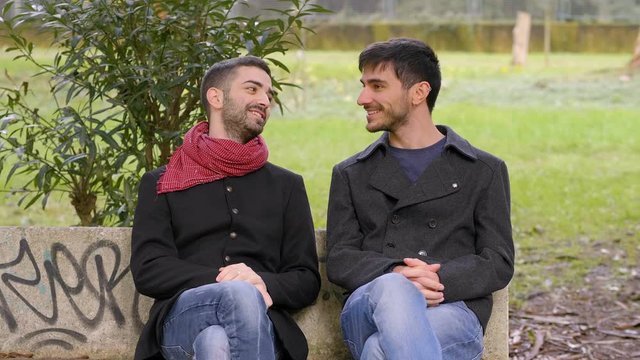 young attractive gay trying to hug his embarassed friend in a bench at park