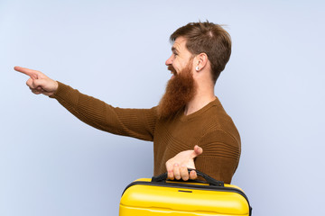 Redhead man with long beard holding a suitcase pointing to the side to present a product