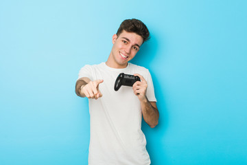 Fototapeta na wymiar Young caucasian man playing videogames with game controller cheerful smiles pointing to front.