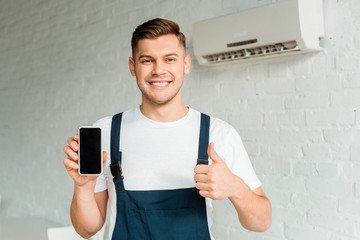 cheerful installer showing thumb up while holding smartphone with blank screen