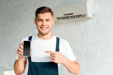 cheerful installer pointing with finger at smartphone with blank screen