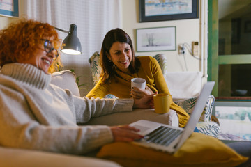 two woman friends using laptop computer at home