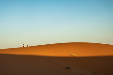 Dos personas caminando sobre dunas en el desierto al atardecer. Erg Chebbi, Marruecos.