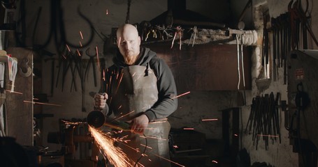 Blacksmith with angle grinder in his workshop sparks flying