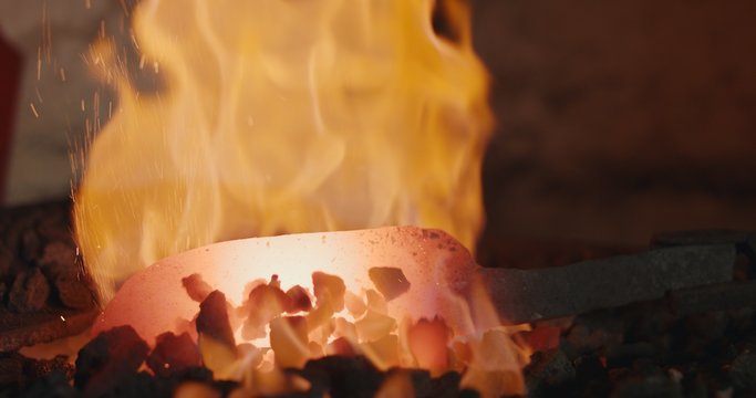 Blacksmith forging iron in open fire making a knife