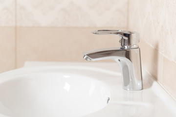 Water tap faucet with running water in a white bathroom sink.