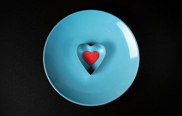 Fototapeta premium Red heart in a metal shape on a blue plate on a black background, concept for Valentine's Day, wedding, birthday and other holidays, view from the top.