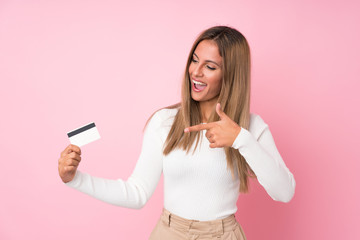 Naklejka premium Young blonde woman over isolated pink background holding a credit card