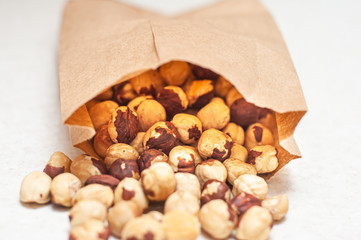 Poured beautifully laid out hazelnuts from a brown paper bag on a white table.