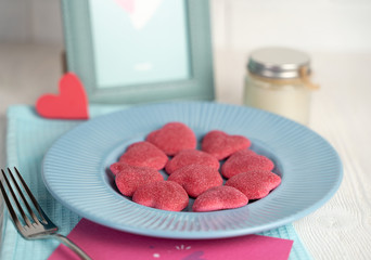 Marmalade pink hearts on a blue plate with ribbed edges on the background of a frame on a light beige wooden background, a concept for Valentine's Day, wedding, birthday and other holidays, a view fro