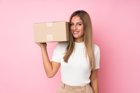 Young blonde woman over isolated pink background holding a box to move it to another site