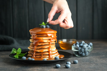Delicious pancakes, with fresh blueberries, strawberries and caramel on a dark background.