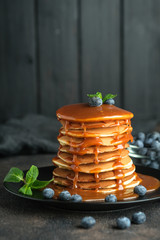 Delicious pancakes, with fresh blueberries, strawberries and caramel on a dark background.
