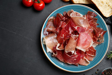 Tasty prosciutto served on black table, flat lay