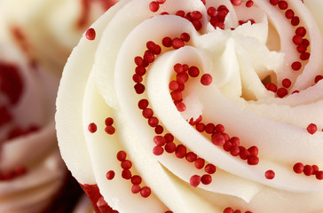 Closeup of red velvet cupcake decorated with swirled icing and sugar beads