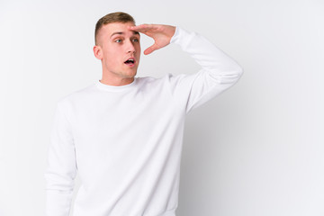 Young caucasian man on white background looking far away keeping hand on forehead.