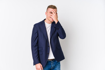 Young business caucasian man blink at the camera through fingers, embarrassed covering face.