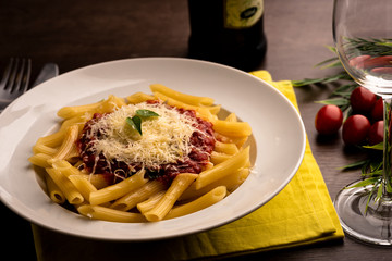 Penne pasta in bolognese sauce in white dish on yellow cloth on wooden table