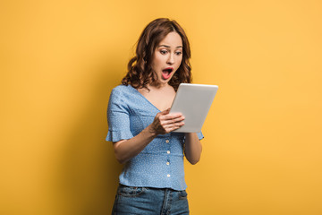 shocked woman using digital tablet on yellow background