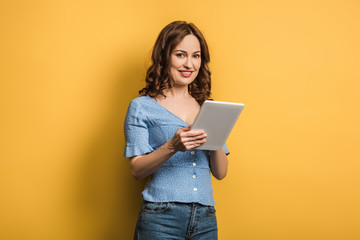 young woman smiling at camera while using digital tablet on yellow background