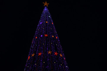 a giant glittering Christmas tree against the dark night sky. new year garlands stars sparkle. low view angle.