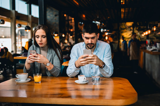 Couple Sitting In Cafe Using Mobile Phones Ignoring Each Other