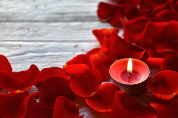 Red rose petals and red burning candle on a white wooden background. St. Valentine's Day background. 