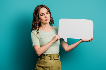 serious girl looking at camera while holding speech bubble on blue background